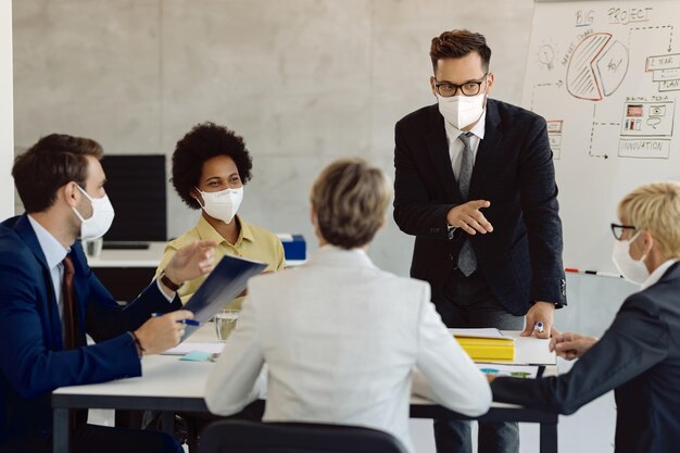 Grupo de colegas de negocios con máscaras faciales haciendo una lluvia de ideas durante una reunión en la oficina