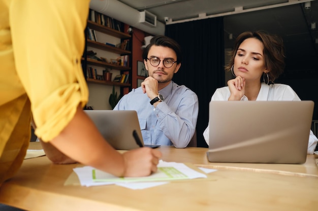 Grupo de colegas de negocios sentados en el escritorio con una computadora portátil mientras trabajan cuidadosamente con papeles en una oficina moderna