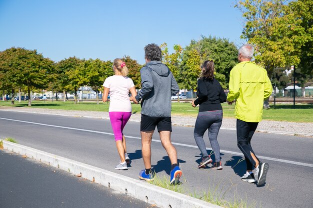Grupo de corredores maduros en ropa deportiva corriendo afuera, entrenando para maratón, disfrutando del entrenamiento matutino. Disparo de cuerpo entero. Personas jubiladas y concepto de estilo de vida activo.