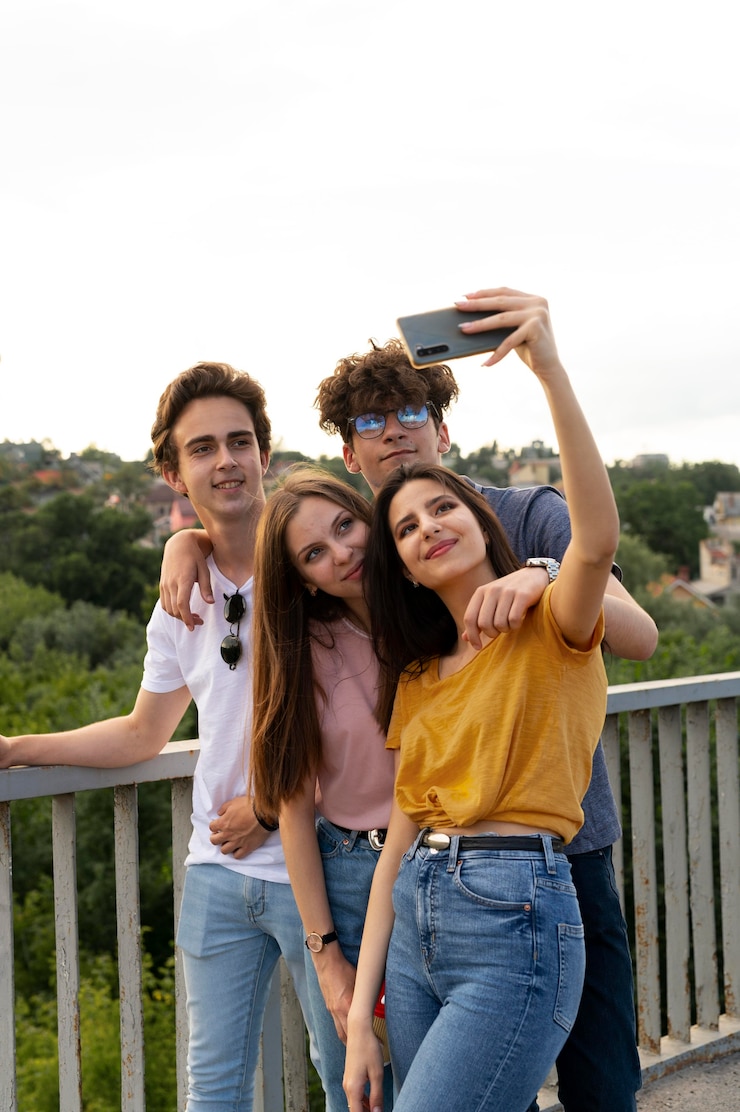 Foto gratuito grupo de cuatro amigos pasando tiempo juntos al aire libre y tomando selfie