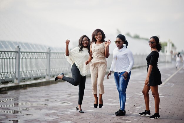 Grupo de cuatro chicas afroamericanas divirtiéndose y saltando contra el lago con fuentes