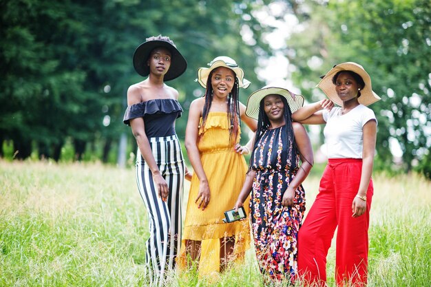Grupo de cuatro hermosas mujeres afroamericanas usan sombrero de verano pasando tiempo en la hierba verde en el parque