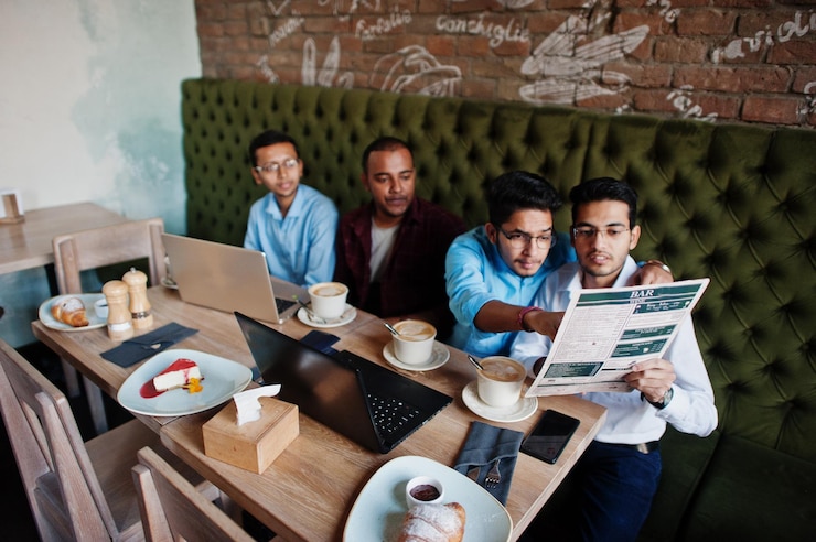Foto gratuito grupo de cuatro hombres del sur de asia posaron en una reunión de negocios en un café los indios trabajan juntos con computadoras portátiles usando varios dispositivos conversando y mirando el menú