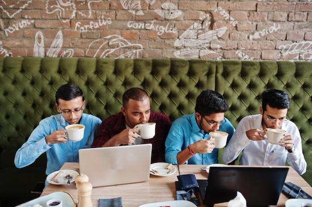 Foto gratuita grupo de cuatro hombres del sur de asia posaron en una reunión de negocios en un café los indios trabajan juntos con computadoras portátiles usando varios dispositivos para conversar y tomar café