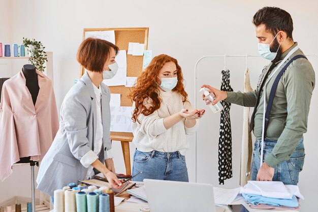 Grupo de diseñadores de moda con máscaras médicas desinfectando las manos mientras trabajaba en el atelier