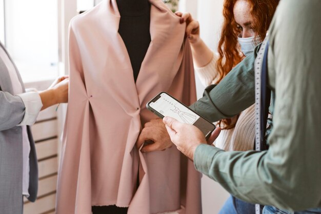 Grupo de diseñadores de moda que trabajan en el atelier y revisan la prenda en forma de vestido