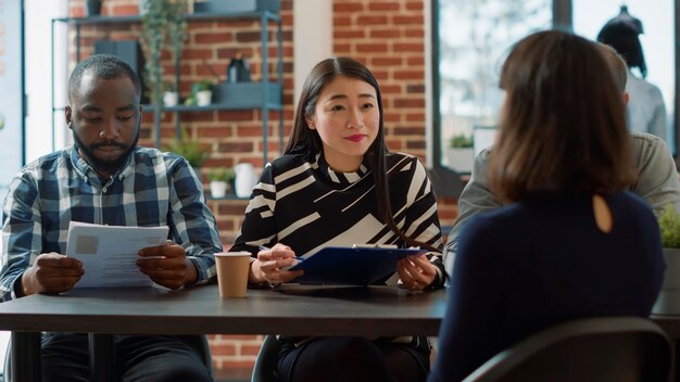 Grupo diverso de empleados hablando con el solicitante en una entrevista de trabajo, preguntando sobre experiencia laboral y experiencia comercial. Equipo de recursos humanos mirando archivos cv y entrevistando a una mujer en la reunión.