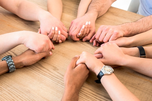 Grupo de diversos amigos sosteniendo sus manos juntas sobre mesa de madera