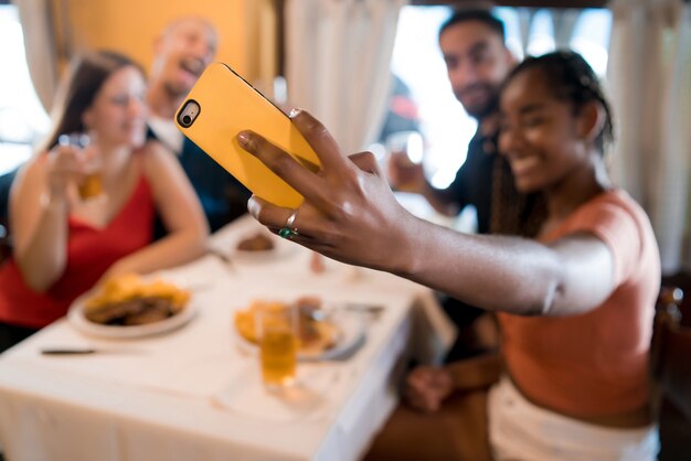 Grupo de diversos amigos tomando un selfie con un teléfono móvil mientras disfrutan de una comida juntos en un restaurante. Concepto de amigos.