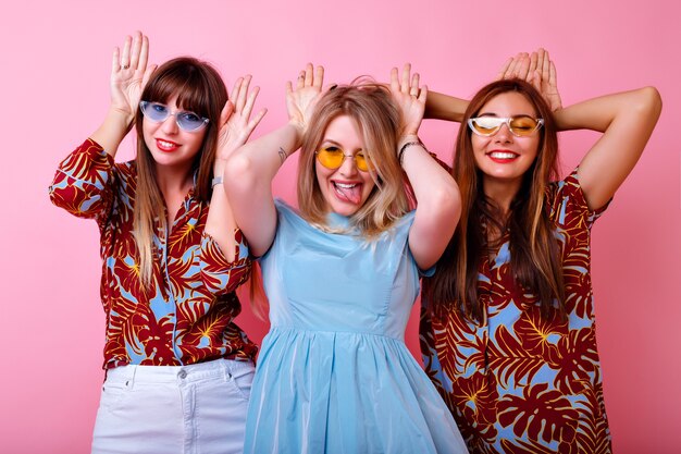 Grupo de divertidas chicas hipster imitando orejas de conejo con sus manos, mostrando la lengua y sonriendo, estilo de fiesta juvenil divertida, ropa de verano de moda y gafas coloridas