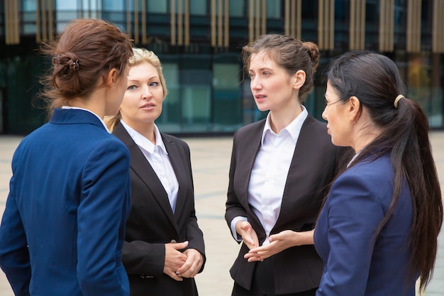 Grupo empresarial femenino de intercambio de ideas al aire libre. Empresarias con trajes de pie juntos en la ciudad y hablando.