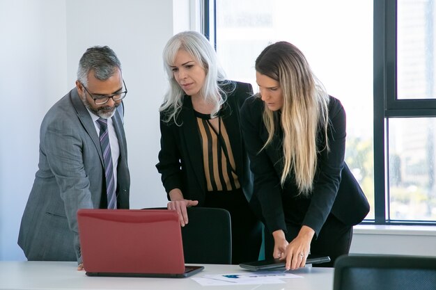 Grupo empresarial viendo la presentación del proyecto, de pie en la mesa de reuniones, mirando la pantalla del portátil. Tiro medio. Concepto de comunicación empresarial