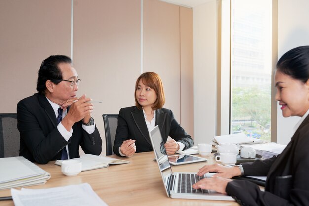 Grupo de empresarios asiáticos sentados alrededor de la mesa de reuniones y hablando