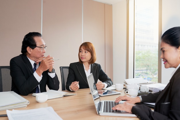 Grupo de empresarios asiáticos sentados alrededor de la mesa de reuniones y hablando