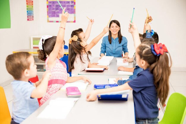 Grupo de estudiantes de preescolar levantando la mano durante la clase y tratando de participar