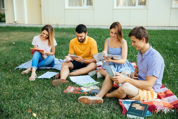 Grupo de estudiantes que estudian sentado en la hierba con cuadernos