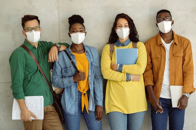 Grupo de estudiantes universitarios con mascarillas protectoras mientras están de pie contra la pared