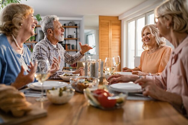 Grupo de felices amigos mayores almorzando juntos y hablando en la mesa del comedor