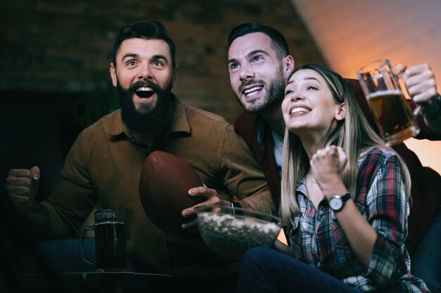 Grupo de gente alegre viendo el partido de rugby en la televisión y animando a su equipo