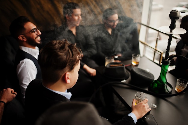 Foto gratuita grupo de guapos gángsters retro bien vestidos pasan tiempo en el club fumando narguile fiesta de la mafia de soltero multiétnico en el restaurante