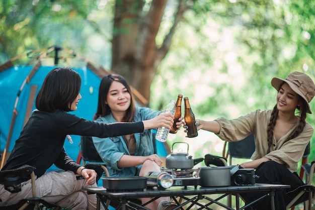 Grupo hermosas mujeres asiáticas amigas viajeras relajándose frente a la tienda de campaña Disfrutan hablando y bebiendo cerveza con diversión y felicidad juntas