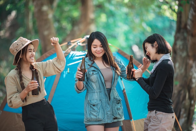 Grupo hermosas mujeres asiáticas amigas viajeras relajándose frente a la tienda de campaña Disfrutan hablando y bebiendo cerveza con diversión y felicidad juntas