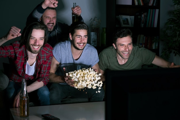 Grupo de hombres comiendo palomitas de maíz y viendo fútbol en la televisión