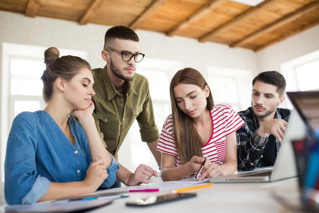 Grupo de hombres y mujeres de negocios que trabajan cuidadosamente con una computadora portátil mientras pasan tiempo en el trabajo Jóvenes creativos discutiendo el trabajo juntos en la oficina moderna