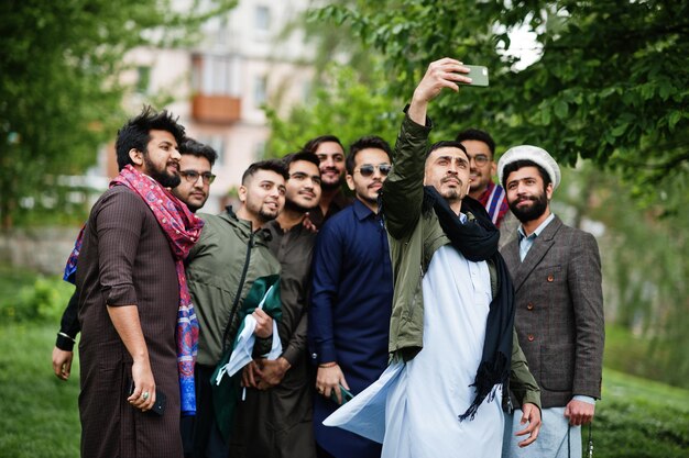 Grupo de hombres pakistaníes con ropa tradicional salwar kameez o kurta haciendo selfie en teléfono móvil
