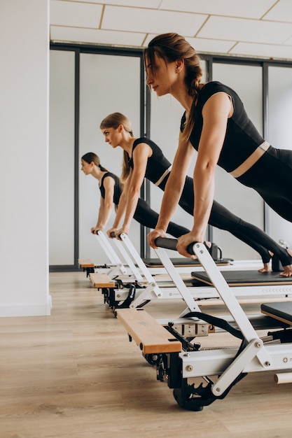 Foto gratuita grupo de instructores de pilates haciendo ejercicio en reformadores