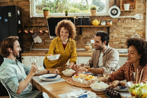 Grupo de jóvenes adultos felices disfrutando durante la hora del almuerzo en la mesa del comedor.