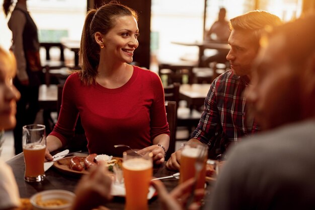 Grupo de jóvenes almorzando y hablando entre ellos en un pub El foco está en la mujer feliz