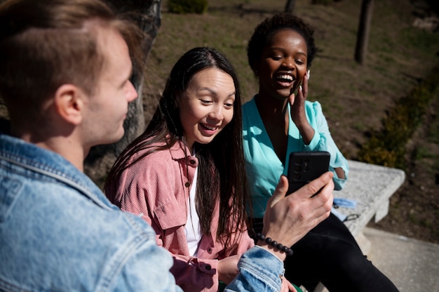 Grupo de jóvenes amigos celebrando el levantamiento de las restricciones de mascarillas al aire libre y usando teléfonos inteligentes