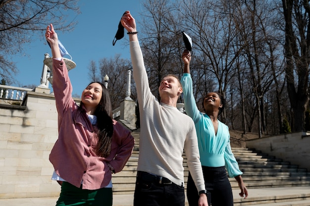 Grupo de jóvenes amigos celebrando el levantamiento de las restricciones de mascarillas en el parque