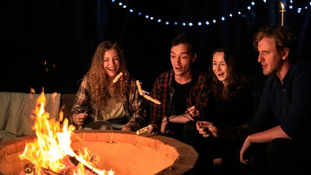 Un grupo de jóvenes amigos felices cerca de una fogata en la noche de glamping