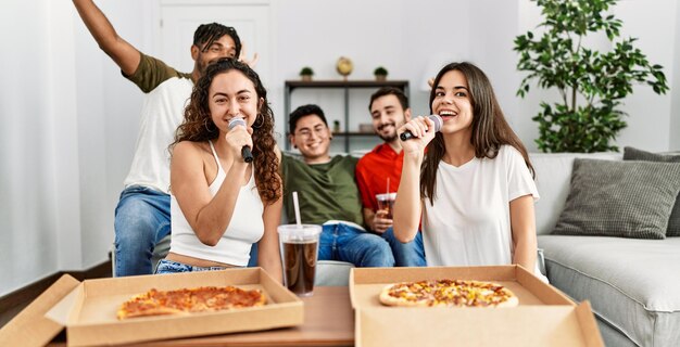 Grupo de jóvenes amigos de fiesta comiendo pizza italiana y cantando canciones en casa