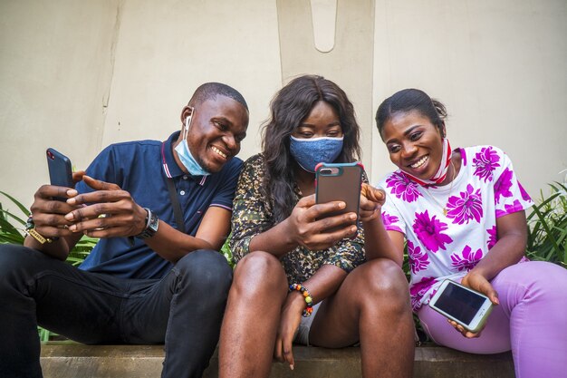 Grupo de jóvenes amigos en mascarillas protectoras usando sus teléfonos al aire libre