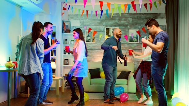 Grupo de jóvenes bailando juntos en una fiesta con luces de neón y buena música. Fiesta universitaria loca