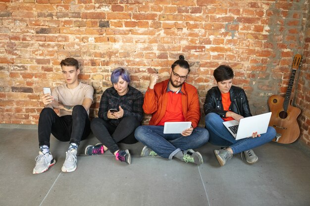 Grupo de jóvenes caucásicos felices sentados detrás de la pared de ladrillo.