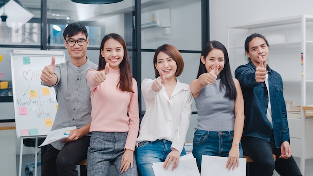 Grupo de jóvenes creativos de Asia en ropa casual elegante sonriendo y pulgar hacia arriba en el lugar de trabajo de la oficina creativa.