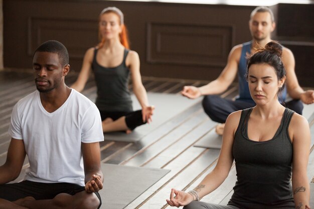 Grupo de jóvenes deportistas meditando en posición de asiento fácil