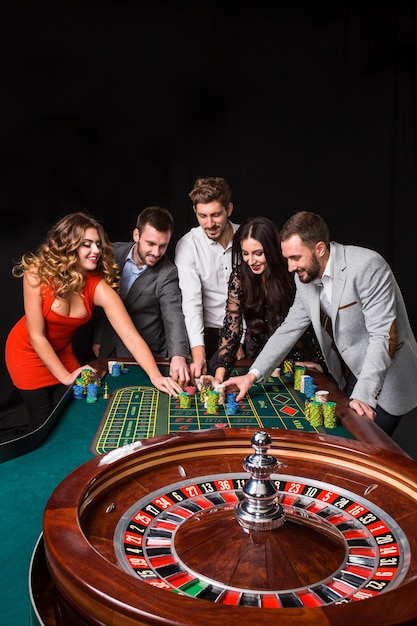 Foto gratuita grupo de jóvenes detrás de la mesa de la ruleta sobre fondo negro. los jóvenes están apostando en el juego.