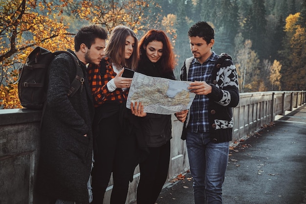 Grupo de jóvenes están mirando el mapa donde están mientras caminan en el bosque de otoño.