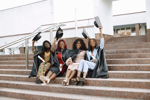 Grupo de jóvenes estudiantes afroamericanas vestidas con toga negra de graduación. Campus como telón de fondo