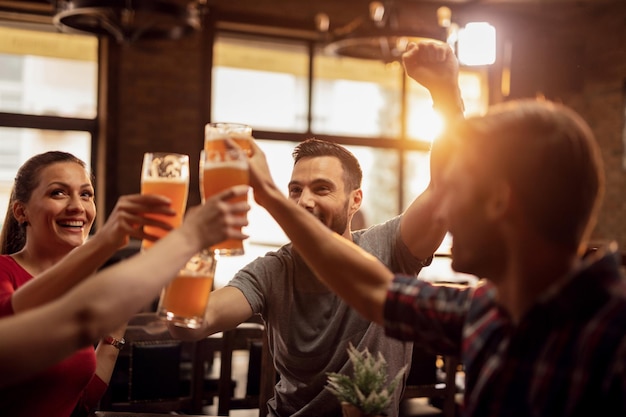 Grupo de jóvenes felices brindando con cerveza y divirtiéndose en un pub