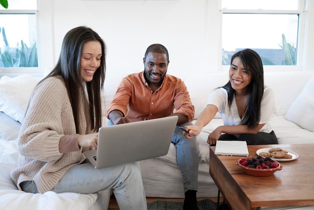 Grupo de jóvenes que usan una computadora portátil juntos en casa en el sofá y toman bocadillos