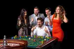 Foto gratuita grupo de jóvenes que se ven emocionados al girar la ruleta. mesa de ruleta en un casino. fondo negro