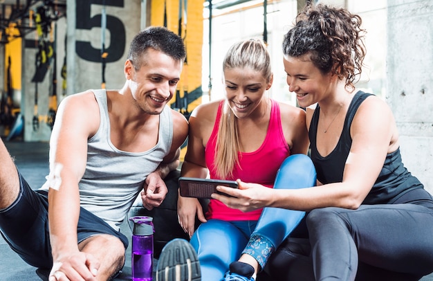 Grupo de jóvenes sonrientes mirando el teléfono celular en el gimnasio