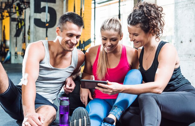 Grupo de jóvenes sonrientes mirando el teléfono celular en el gimnasio