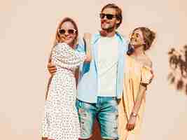 Foto gratuita grupo de jóvenes tres elegantes amigos posando en la calle. hombre de moda y dos chicas lindas vestidas con ropa casual de verano. modelos sonrientes divirtiéndose en gafas de sol. mujeres alegres y un chico volviéndose loco